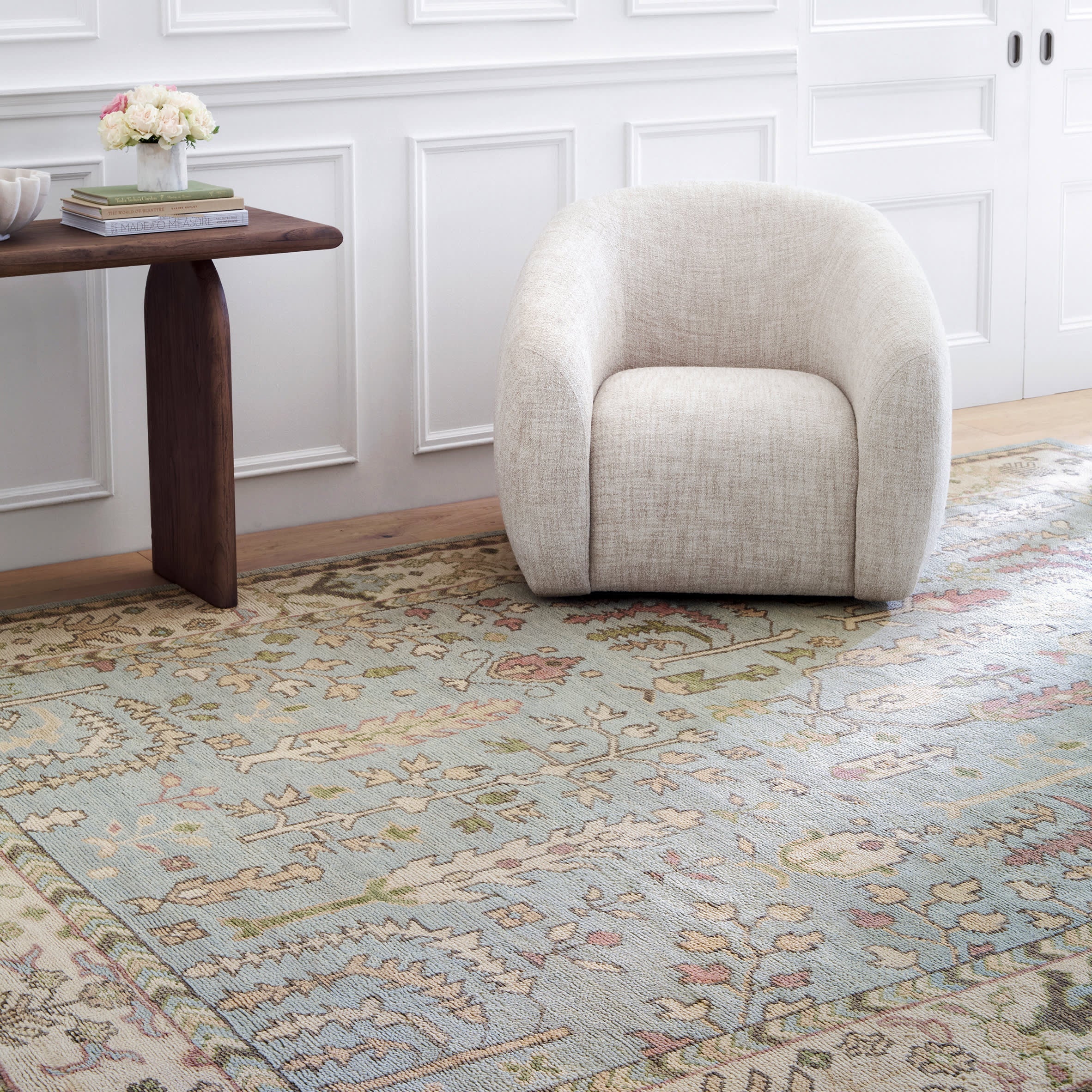 Beige armchair on a patterned rug in a room with wooden table and decorative elements.